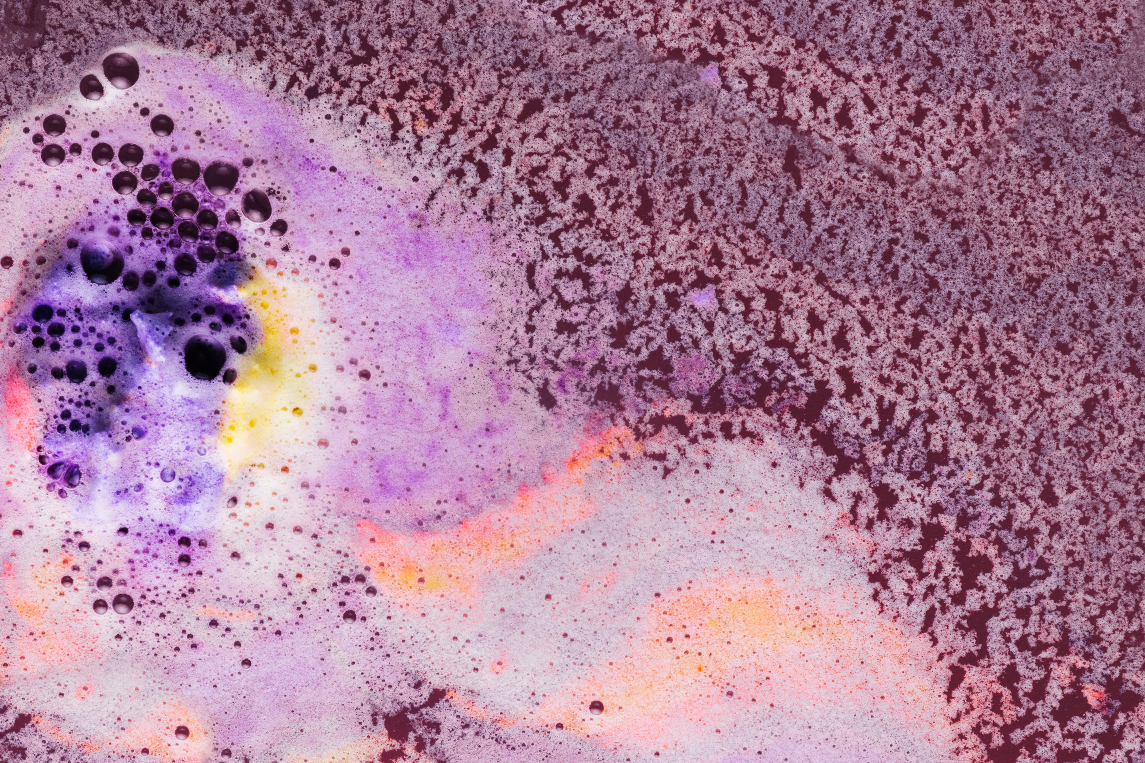 Abstrakte, blasenartige Textur in lebhaften Violett-, Orange- und Gelbtönen, die an eine mikroskopische Aufnahme erinnert.