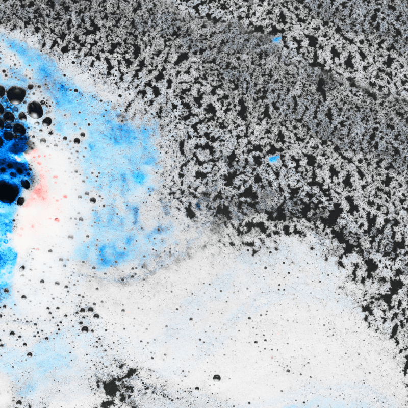 Mikroskopische Aufnahme einer körnigen, texturierten Oberfläche in Schwarz-Weiß mit kontrastierenden hellblauen und leicht rötlichen Farbakzenten und kleinen Bläschen am linken Rand.